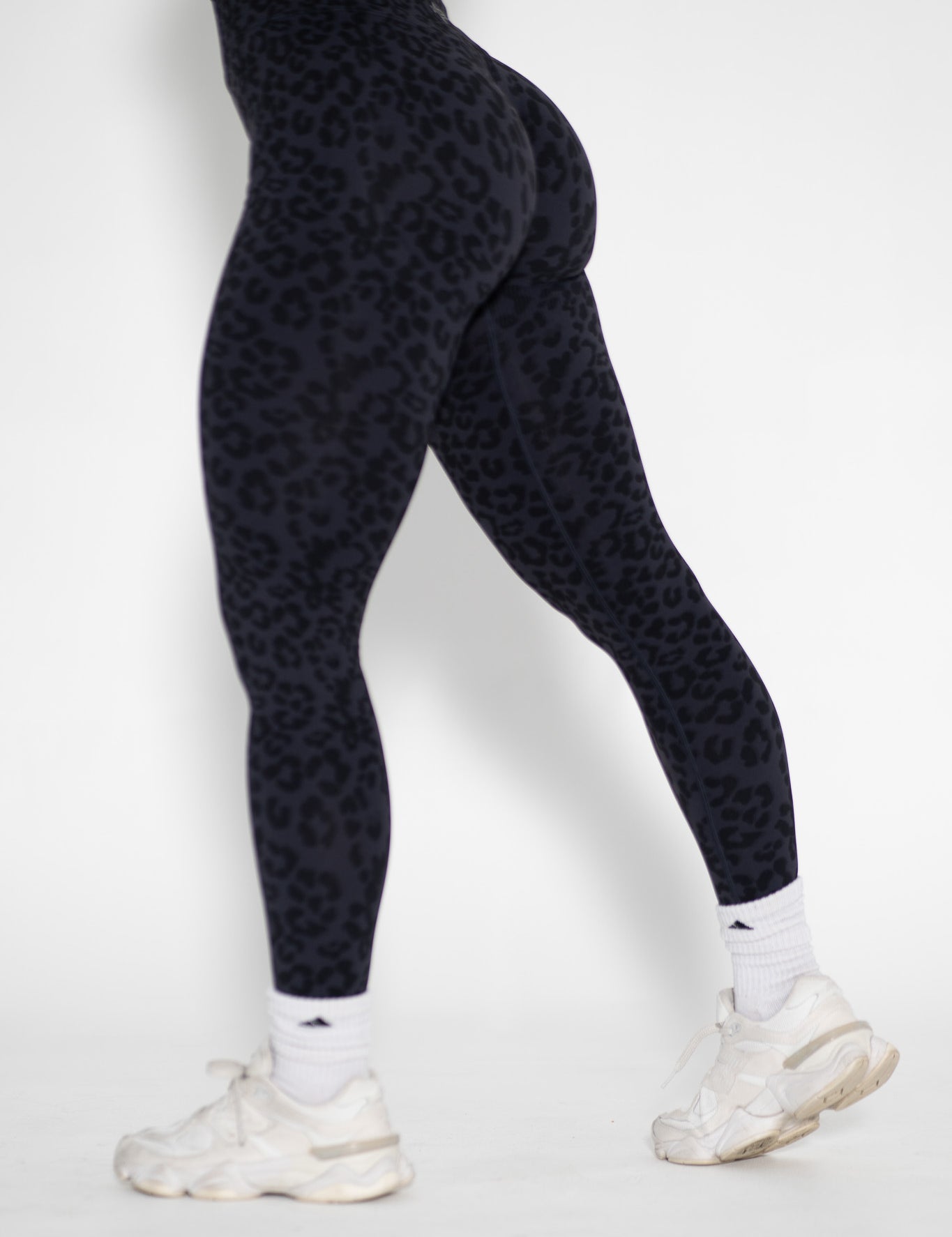 Person wearing black patterned leggings and white sneakers on a white background