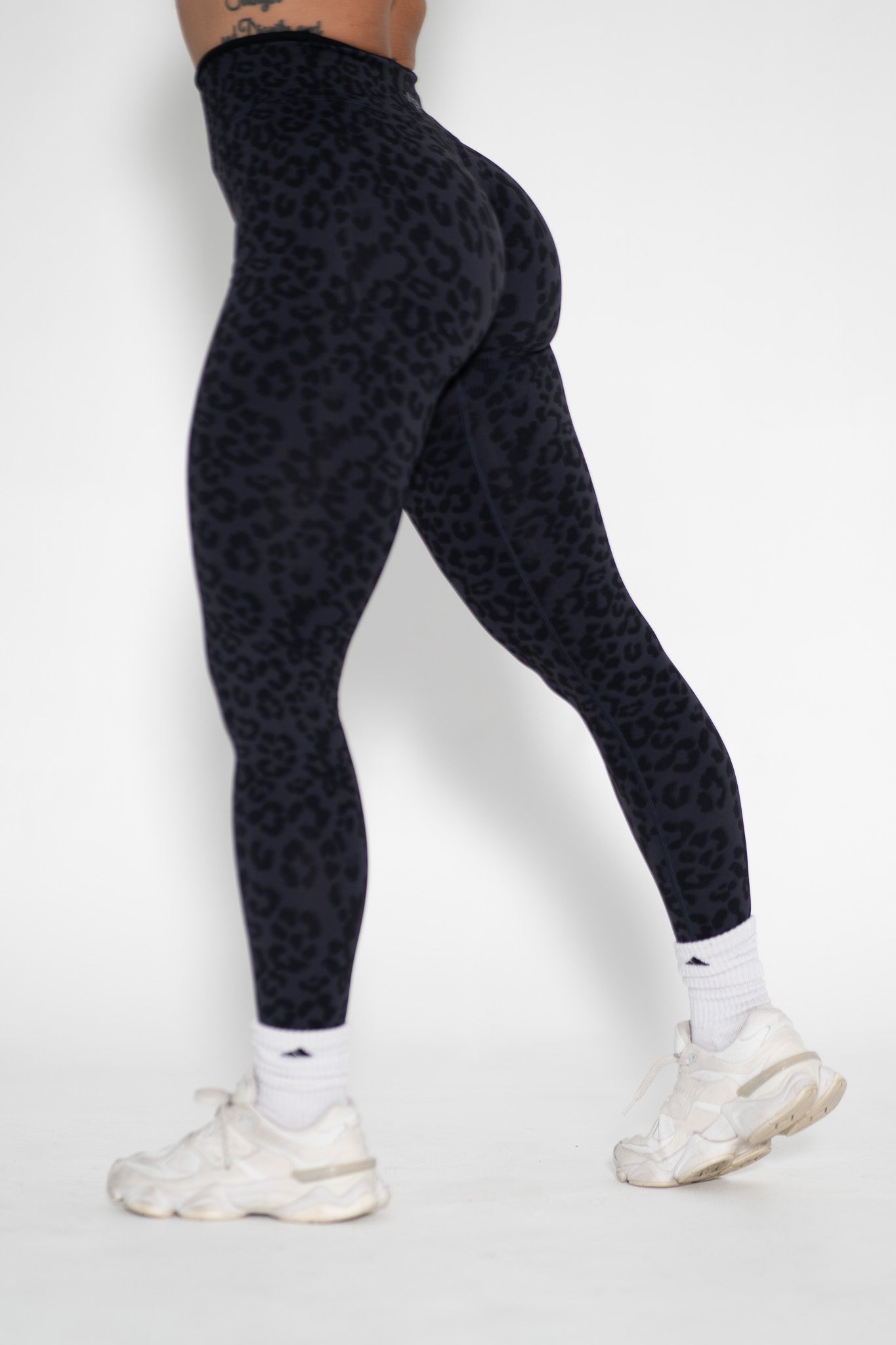 Person wearing black patterned leggings and white sneakers on a white background