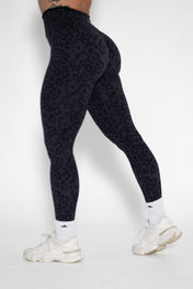 Person wearing black patterned leggings and white sneakers on a white background