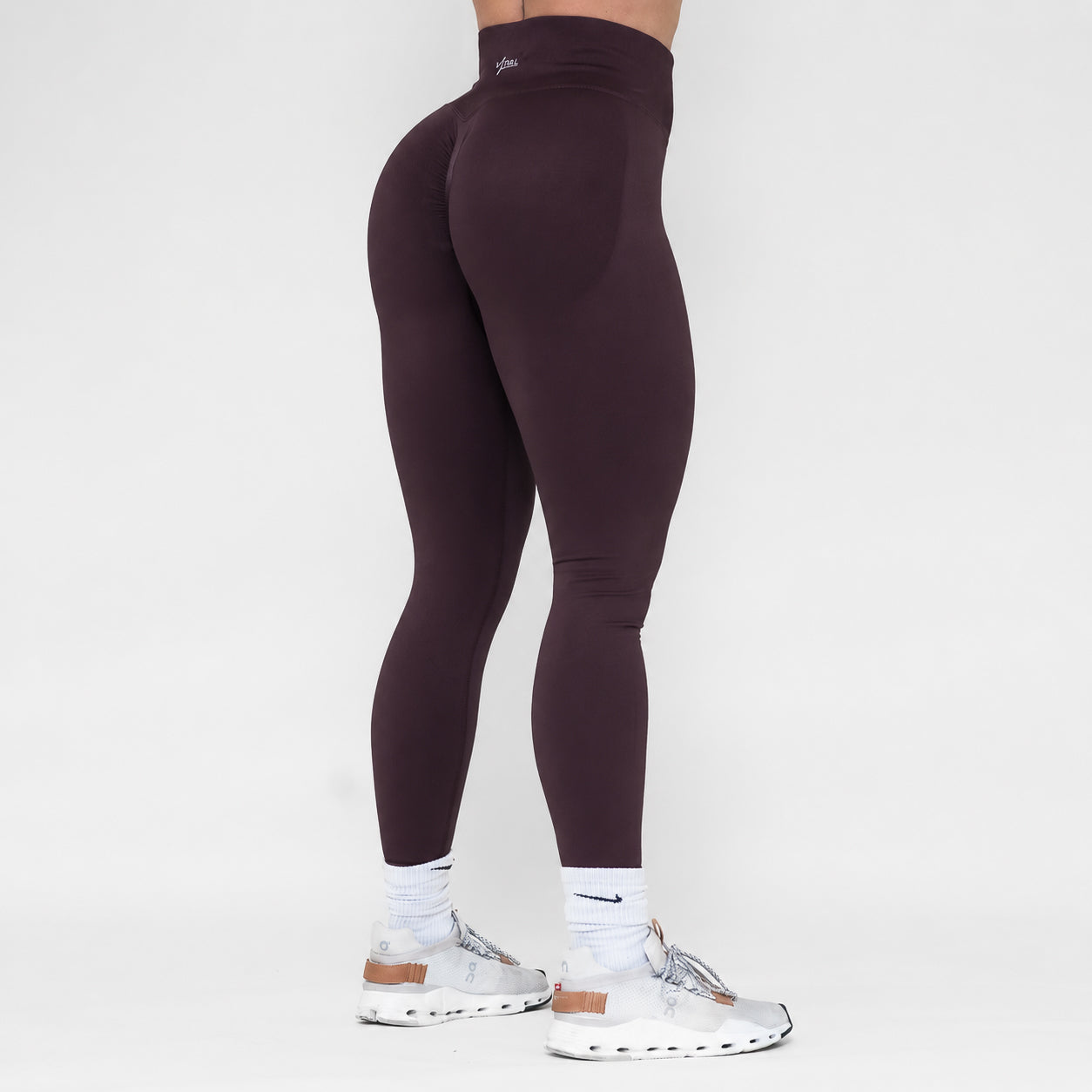 Person wearing dark brown leggings and white sneakers on a white background